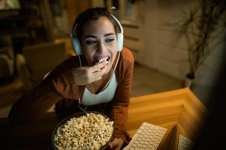 jovem mulher usando fones de ouvido enquanto come pipoca e assiste algo na internet em seu computador em casa 637285 4437