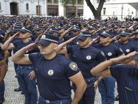 Policiais em uniforme fazem continência durante cerimônia pública em área urbana